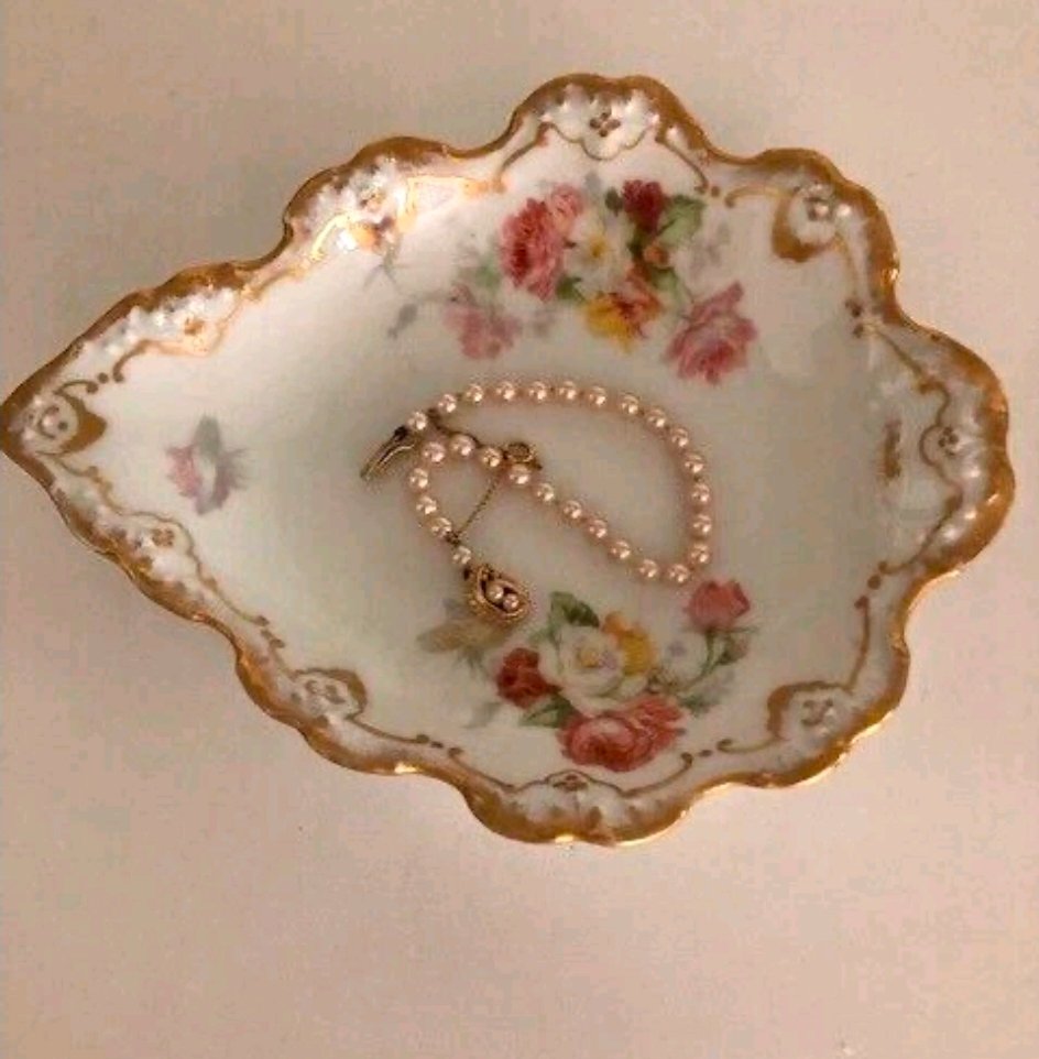 Scalloped porcelain pin dish with heavy gold rim, raised white beading and pink roses, holding a pearl bracelet