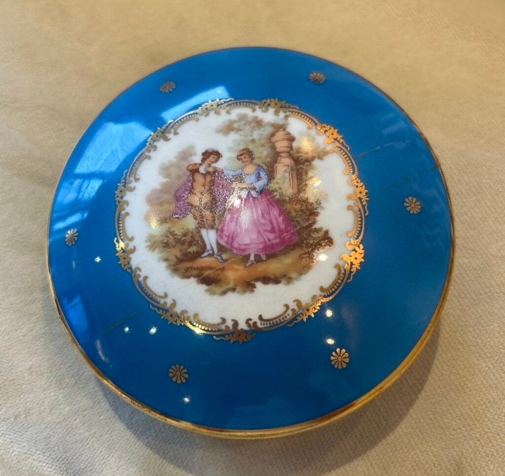 Round porcelain box lid in bright blue with gilt stars and a courting scene in a gilt cartouche