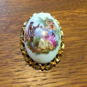 Oval domed porcelain brooch with a musician and lady, in a gilt filigree frame