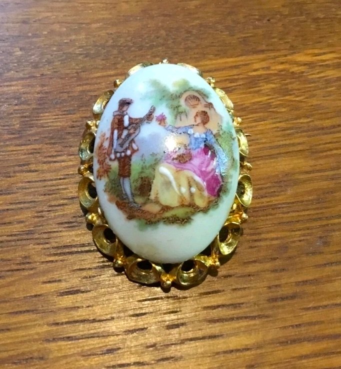 Oval domed porcelain brooch with a musician and lady, in a gilt filigree frame