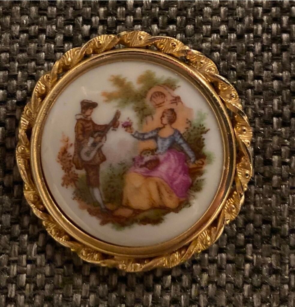 Round porcelain brooch with a guitar player and lady, in a twisted gold frame