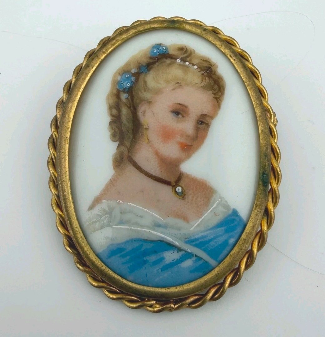 Oval porcelain portrait brooch of a fair-haired woman with blue flowers in her hair, in a rope-twist frame