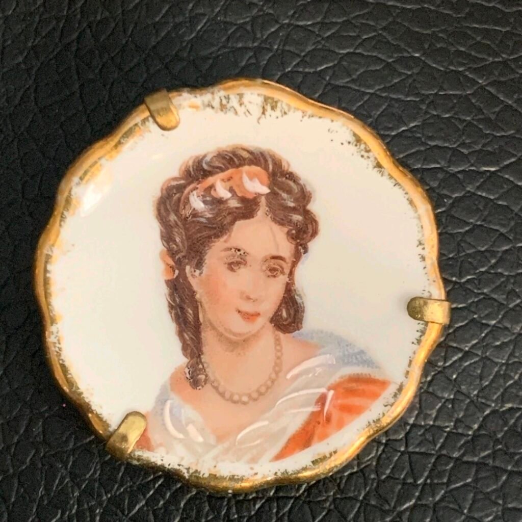 Scalloped porcelain portrait brooch of a dark-haired woman with pearls, with gold rim and prongs