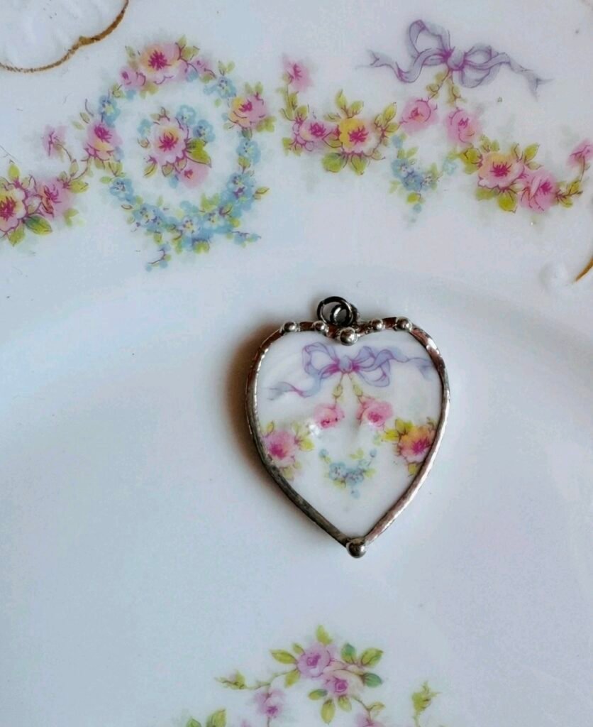Heart-shaped pendant cut from floral porcelain with a lilac bow and pink roses, in a silver-tone frame