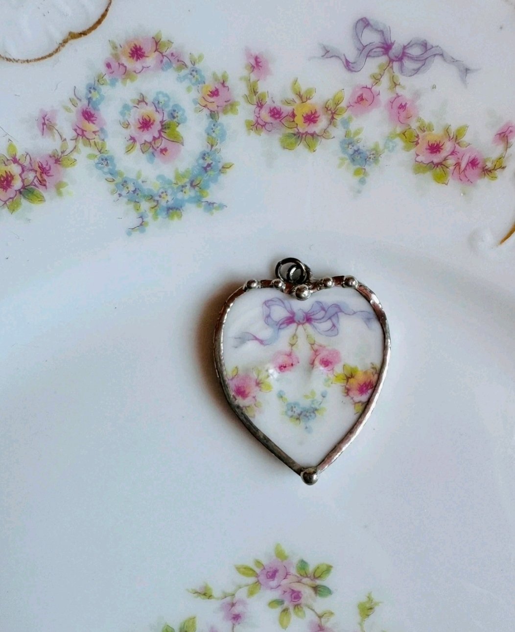 Heart-shaped pendant cut from floral porcelain with a lilac bow and pink roses, in a silver-tone frame